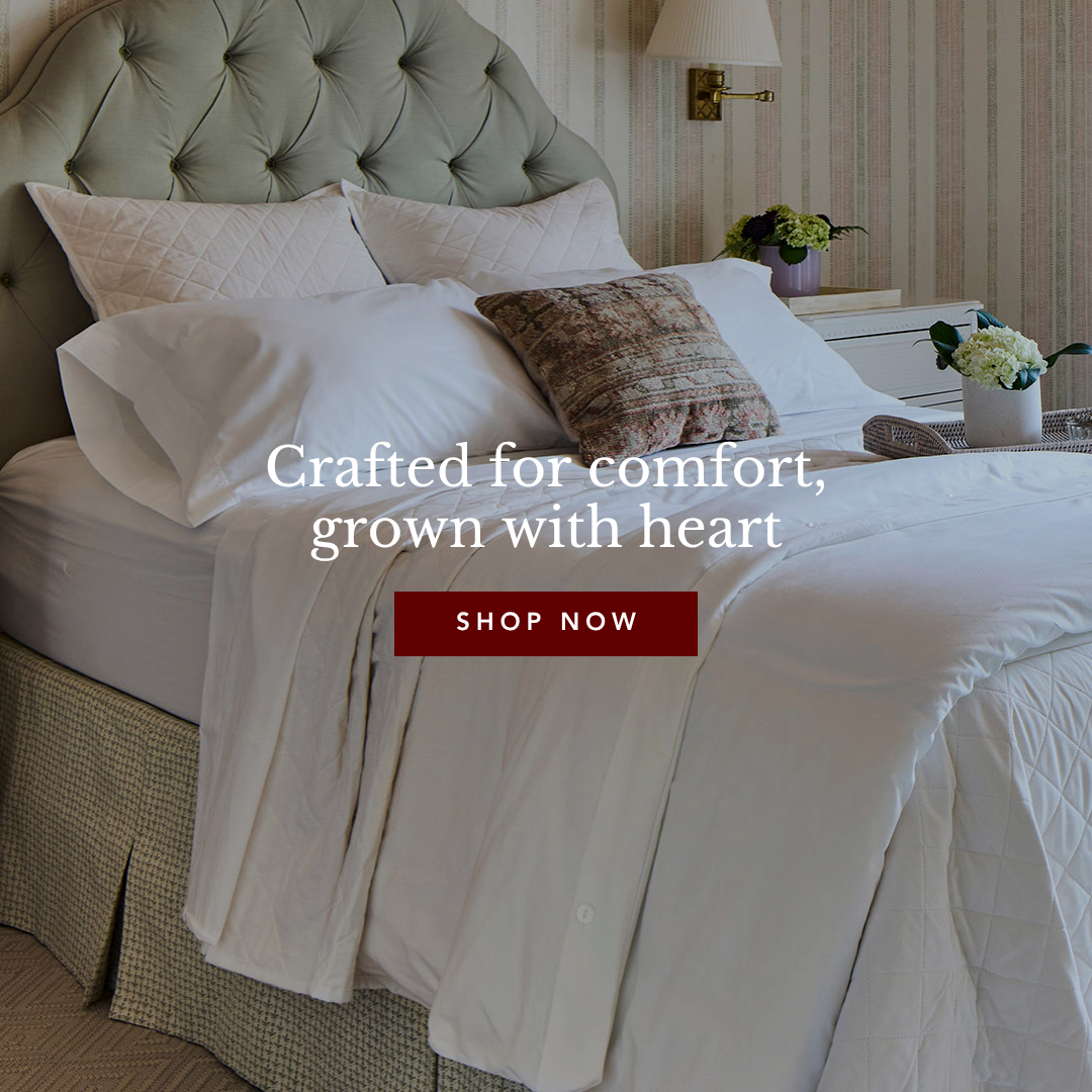 A made bed with white sheets, quilted duvet, and tufted green headboard in a warmly lit bedroom.