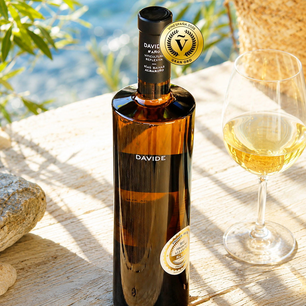 Bottle of Davide Albariño white wine with gold award sticker beside a filled wine glass on a sunlit wooden table by water