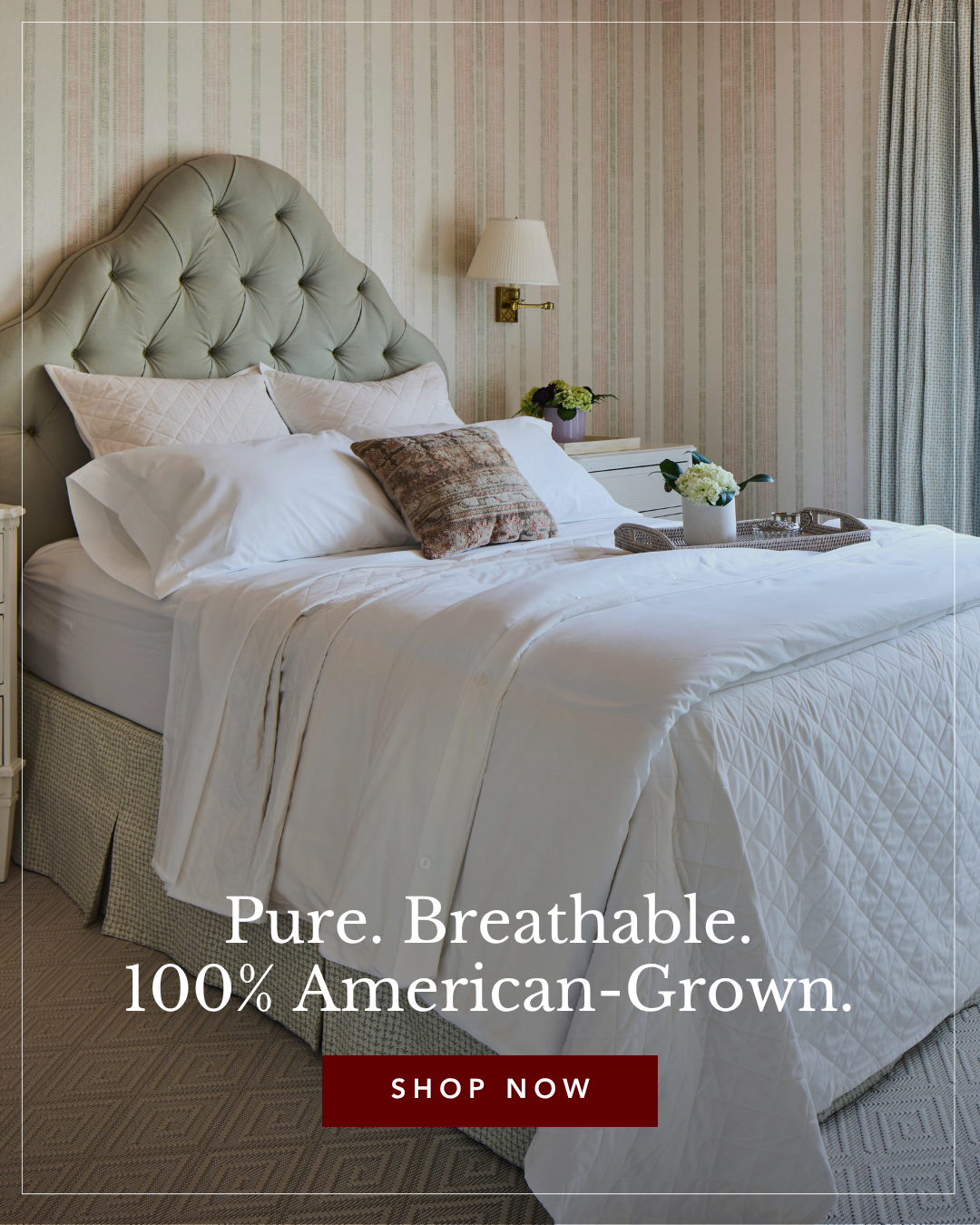 A made bed with white bedding, tufted headboard, and striped wallpaper in a cozy bedroom. A small lamp and floral arrangements are on bedside tables.