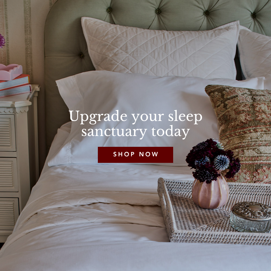 A well-appointed bed with white bedding, fluffy pillows, a tufted green headboard, and a bedside table with decor.