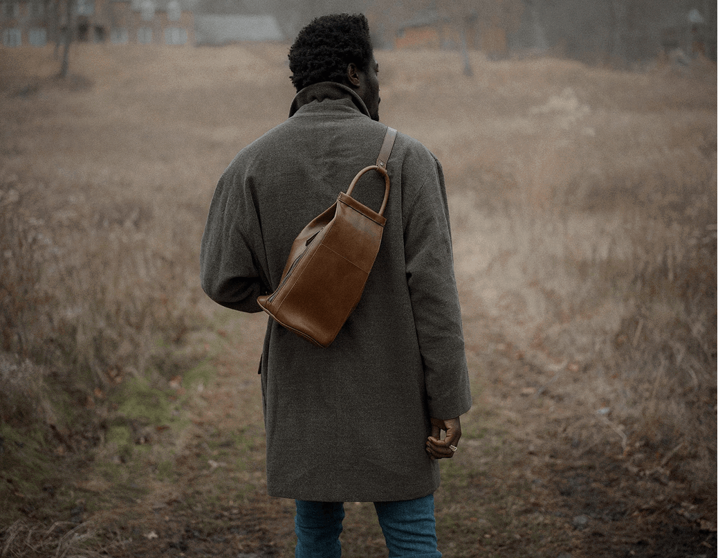 Man walking through a field with leather crossbody sling bag 
