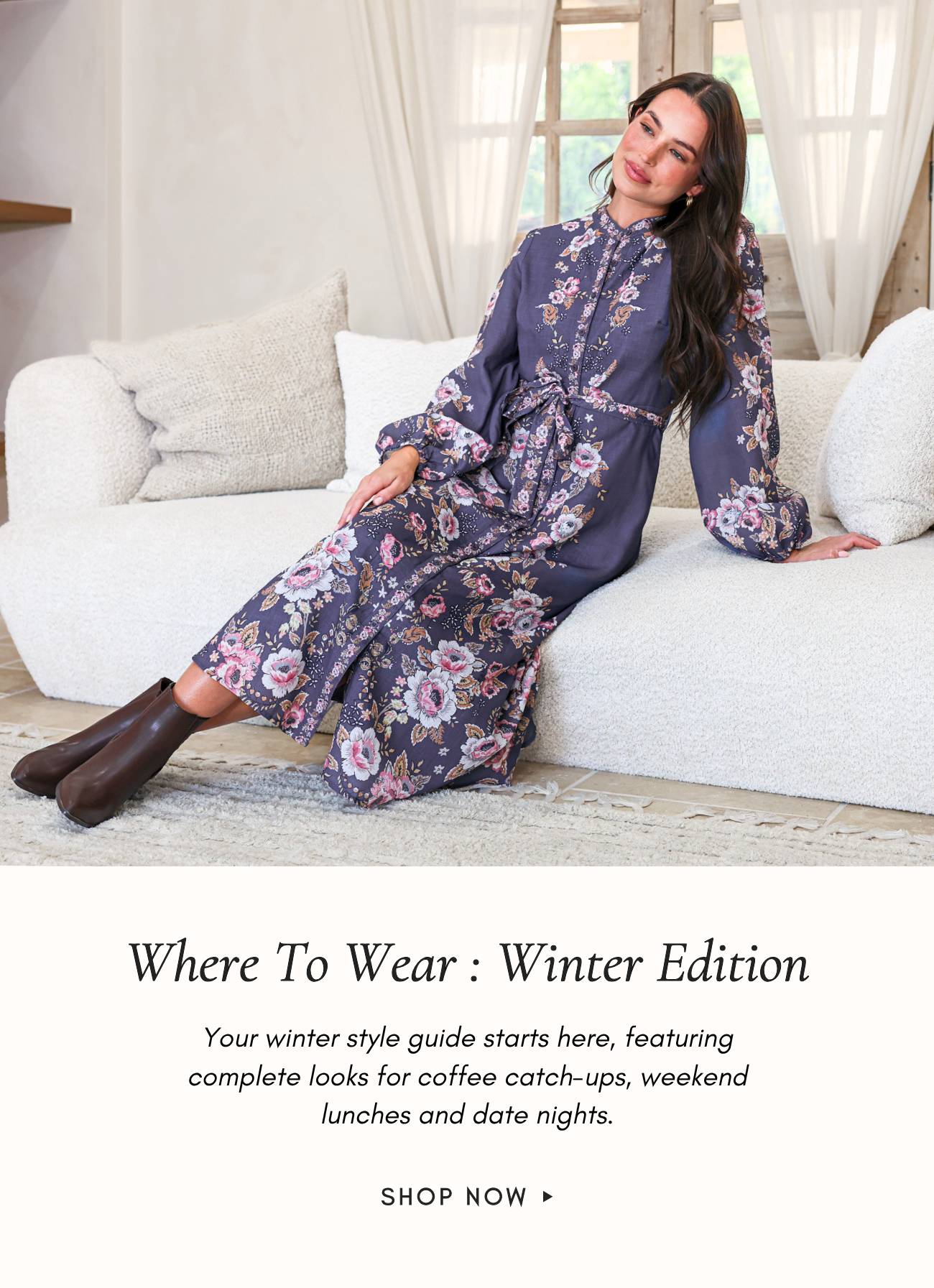 A woman wearing a long-sleeved floral print dress and brown boots sits on a white textured sofa in a brightly lit room with sheer curtains and a windo...