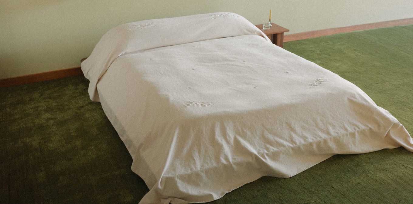 White floral embroidered blanket on a bed in a room with green carpet