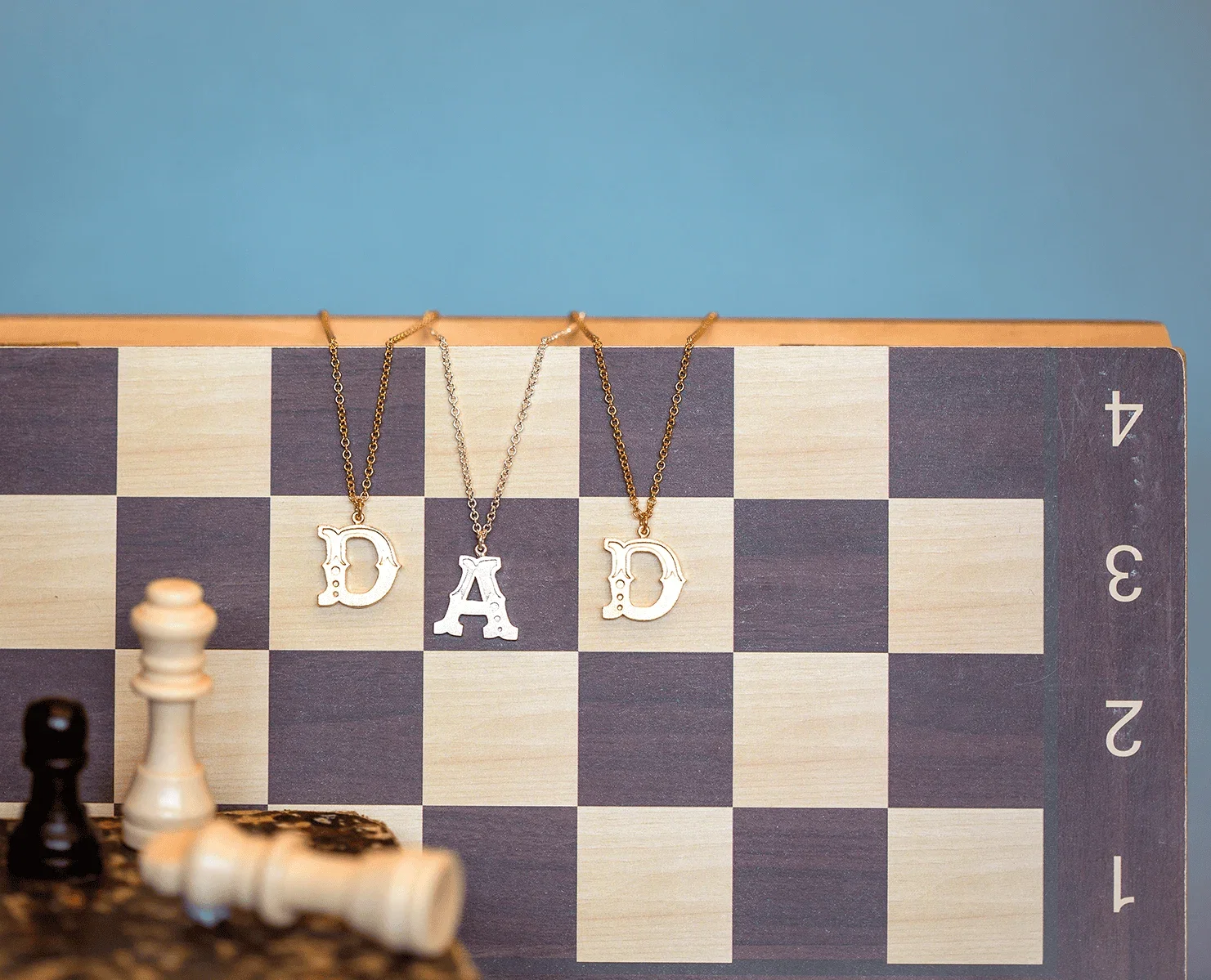 Letter necklaces spelling "DAD" displayed on a chessboard for Father's Day gifting.