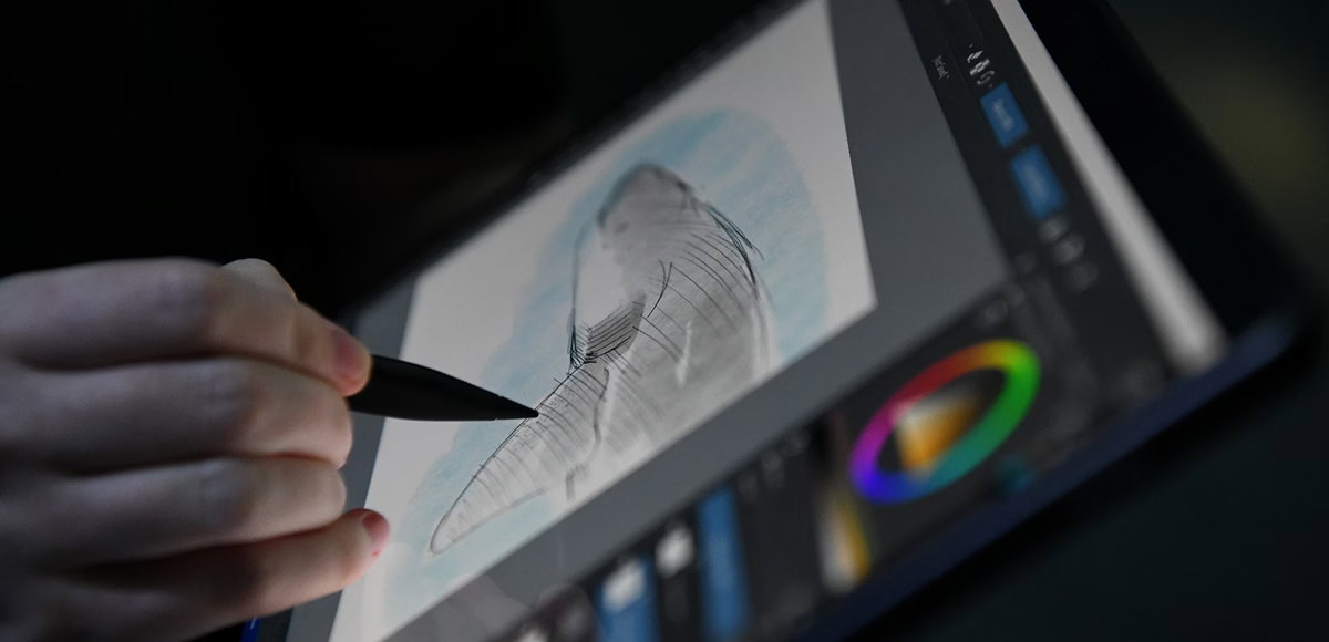 Close-up of a hand using a stylus to sketch a shark on a Surface Pro with digital art tools on screen
