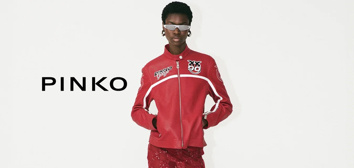 Rote Jacke mit Reißverschluss und Logo-Details, kombiniert mit einem roten Midi-Rock aus Spitze mit einem Schachbrettmuster und weißen High-Heels.