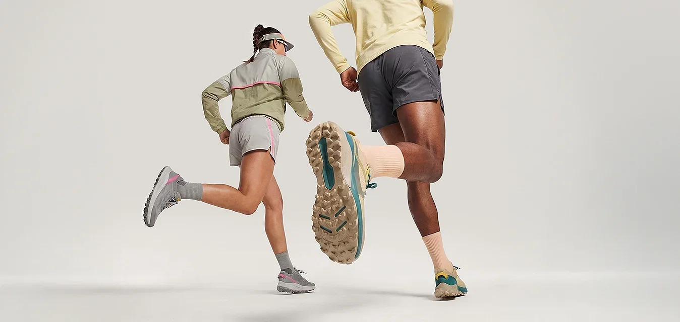 Zwei Personen in Sportbekleidung und Mützen, die auf einem schlichten, hellen Hintergrund nach vorne laufen.