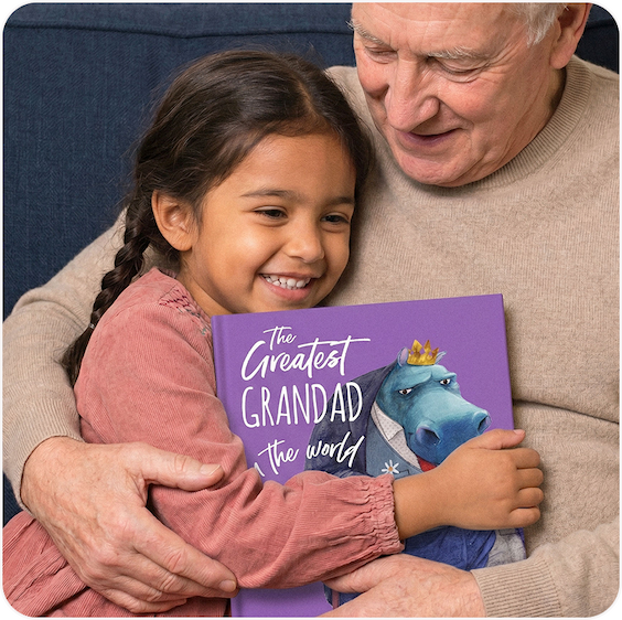 A grandad and young girl sitting together reading a personalised "The Greatest Grandad in the World" book