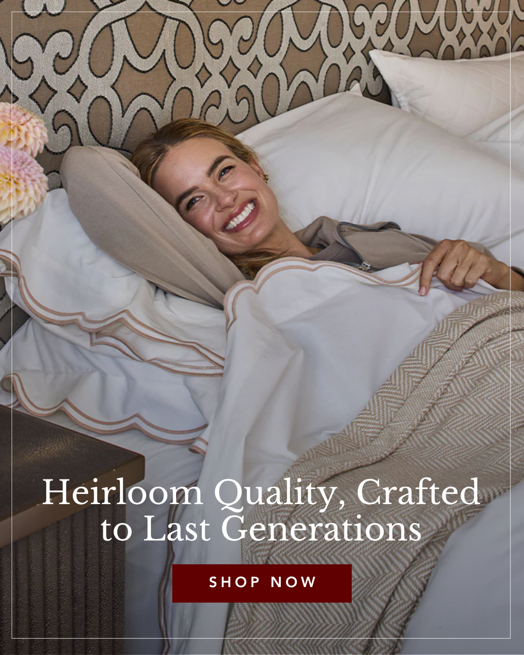 Smiling woman relaxing in a luxurious bed with white bedding, scalloped edges, and an ornate headboard.