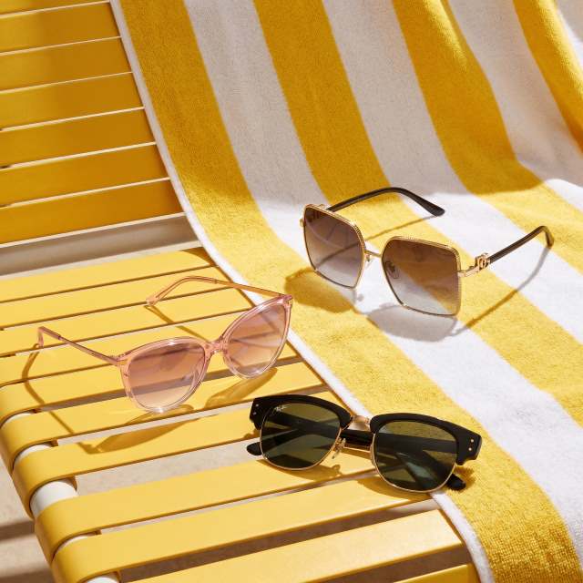 Three pairs of sunglasses on a yellow lounge chair with a striped beach towel.