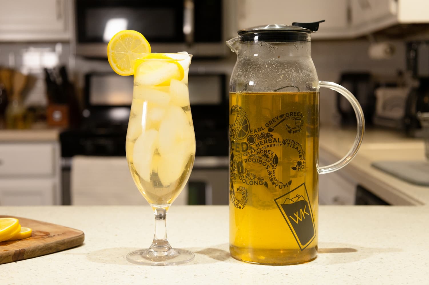 A Decisive Iced Tea Brewer with green iced tea next to a glass of green iced tea topped with a lemon slice
