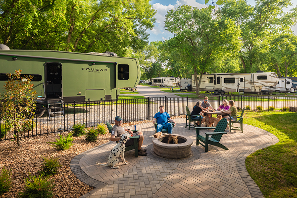 Family and their dog sitting at their KOA patio site with an RV in the background with trees