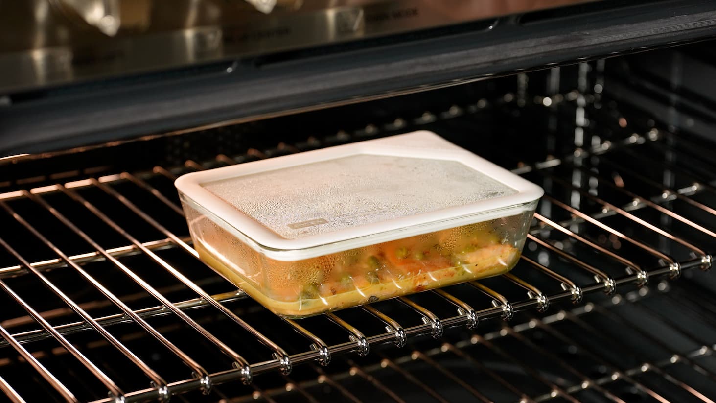 Glass food container with lid baking in an oven on a rack.