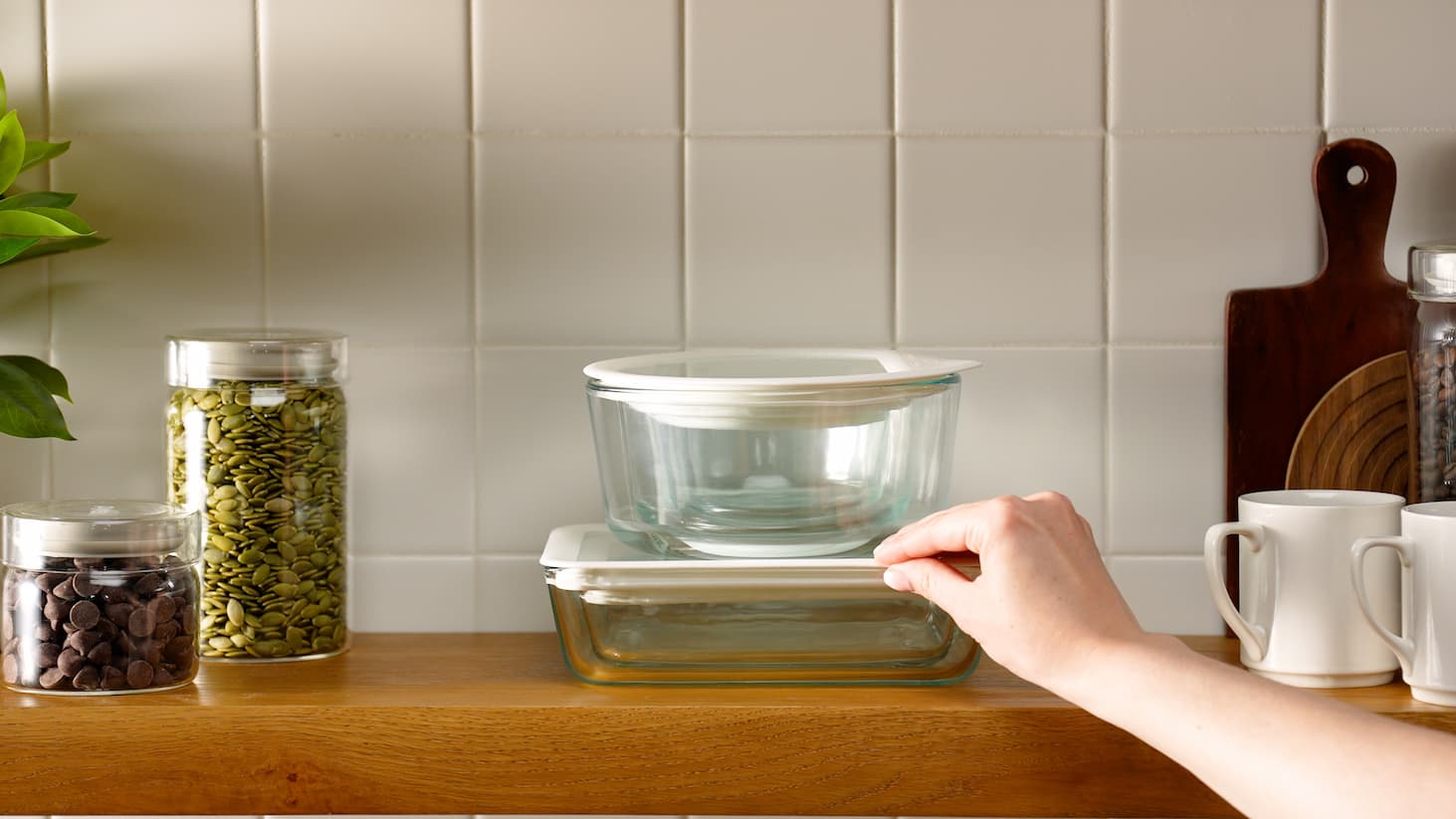 Stackable glass food containers being arranged on a kitchen shelf.