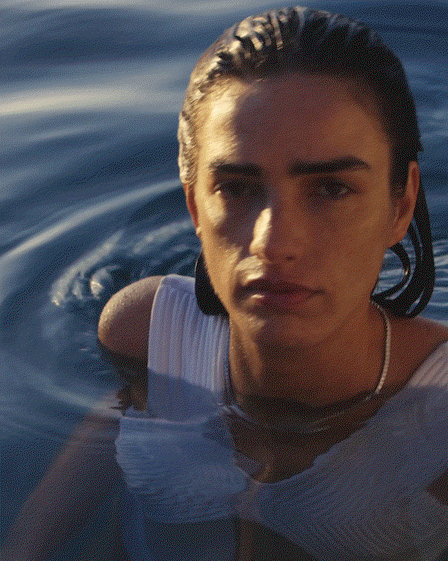 A model wearing a Dorsey rivière necklace stands in open water, hair slicked back, in a white top with rippling blue water behind her.