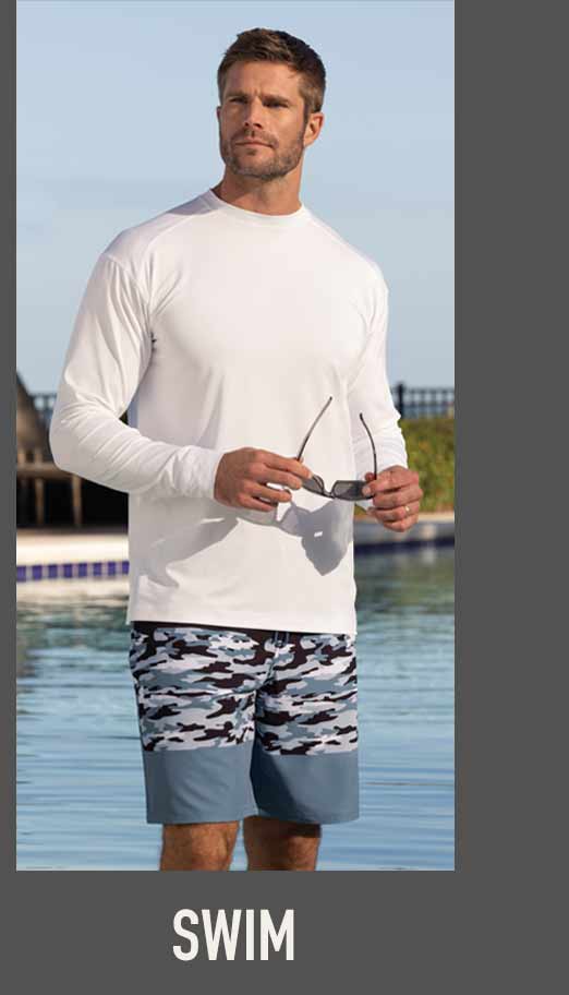 Man standing by a pool wearing a white long-sleeve performance shirt and camo-print swim shorts, holding sunglasses, with Swim label