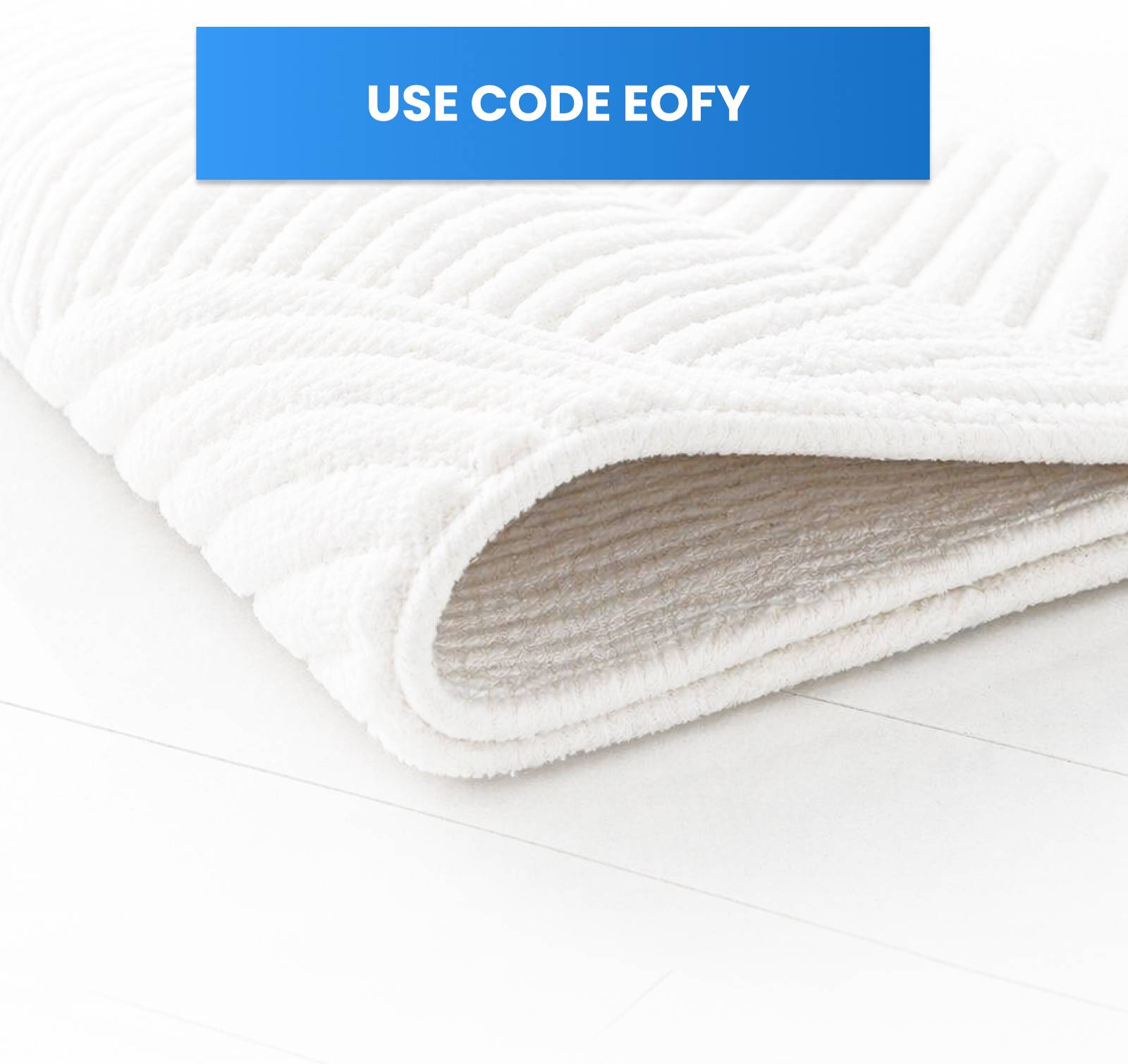 A close-up, angled shot shows a white, textured bath mat with a chevron pattern, partially rolled and resting on a white surface, with a blue banner a...