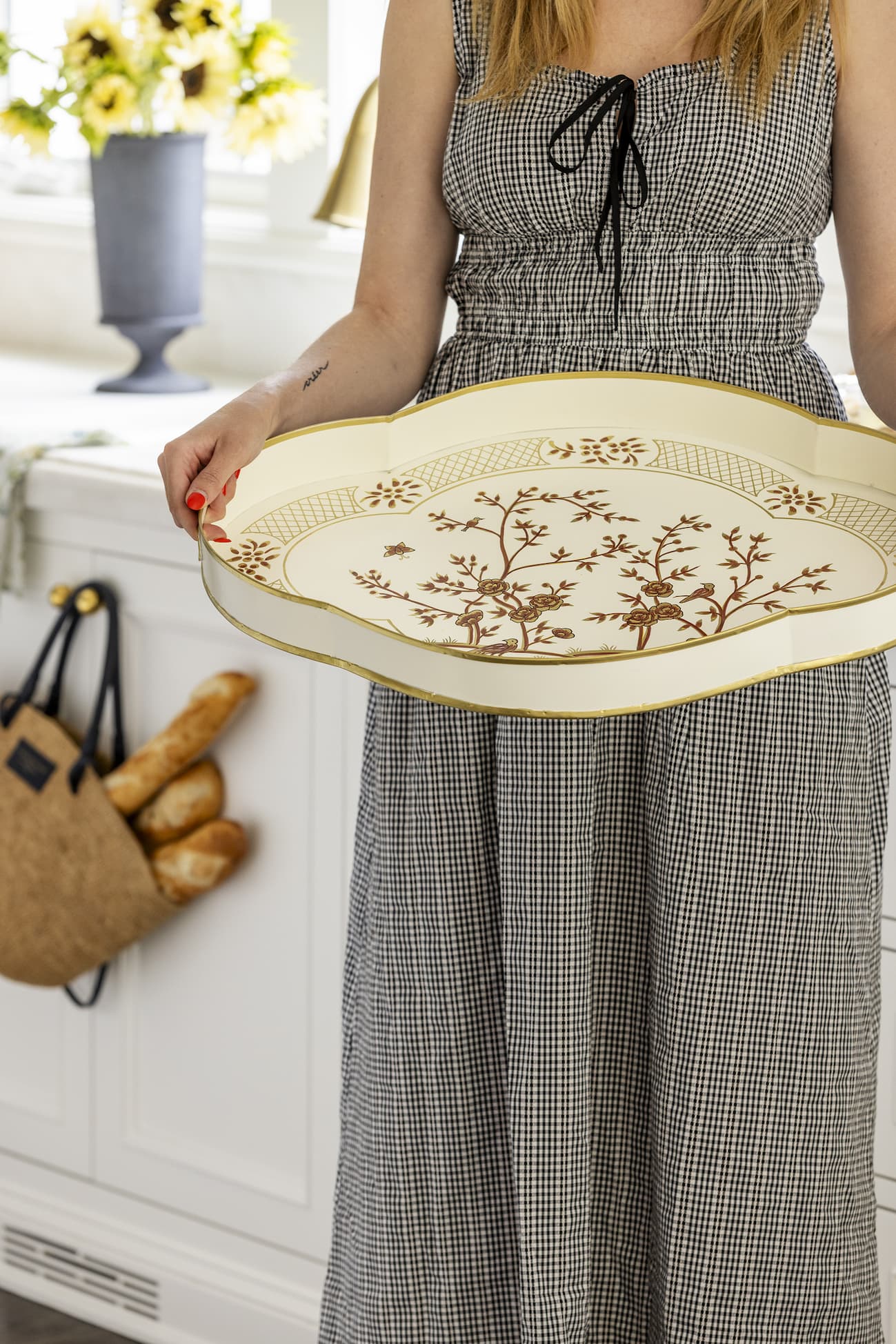 Woman in checkered dress holding serving tray with gold/brown floral detailing.