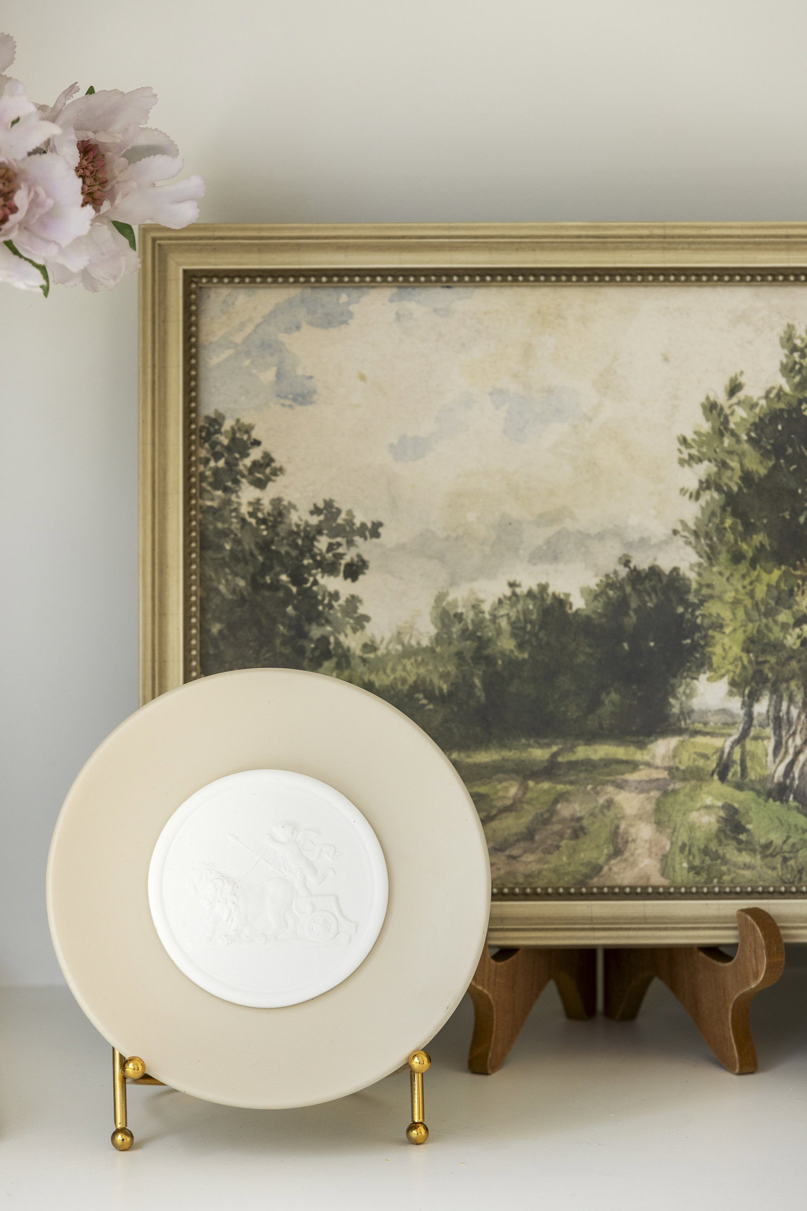 Roman Intaglio on Stand in front of landscape artwork on white shelf.