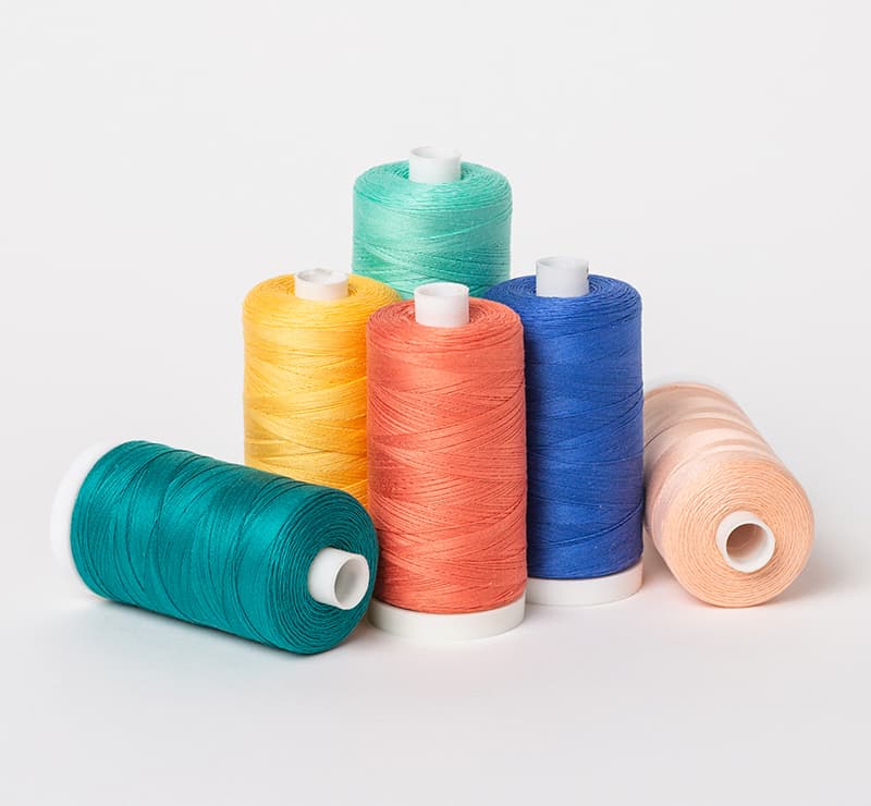 Six spools of sewing and quilting thread in greens, blue, pinks, and yellow. >>