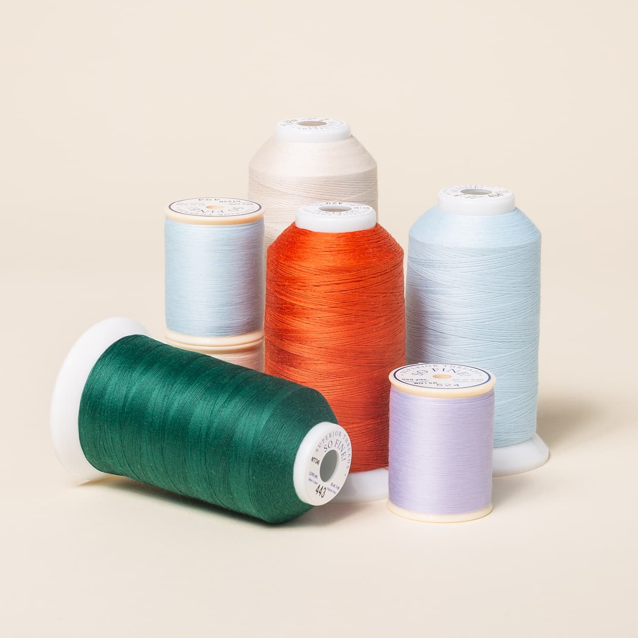 Spools and cones of thread in blues, red, lavender, green, and white. >>