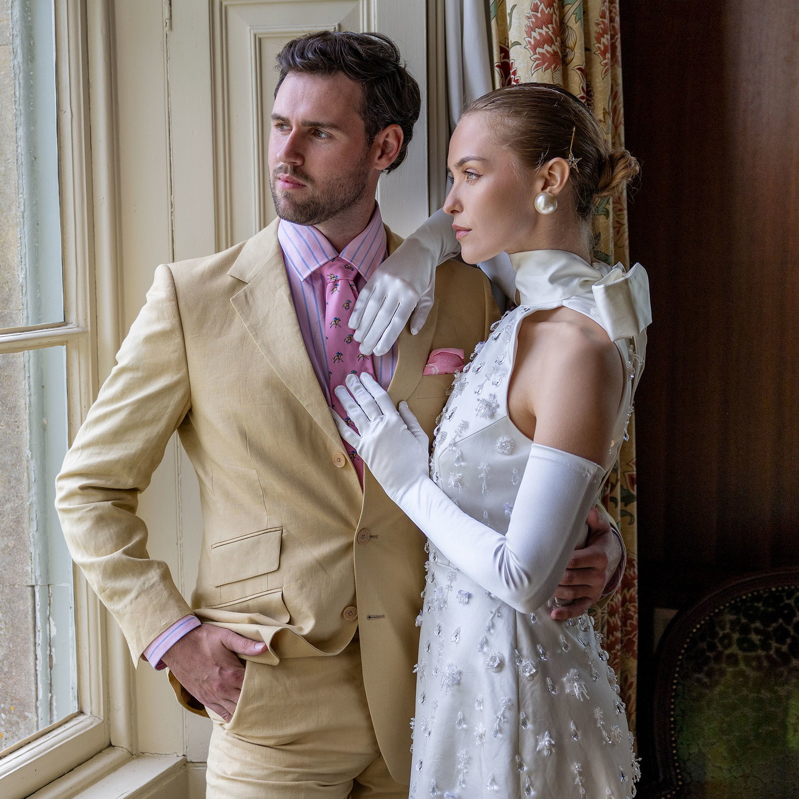Man and woman standing by the window, woman is wearing long satin gloves in ivory