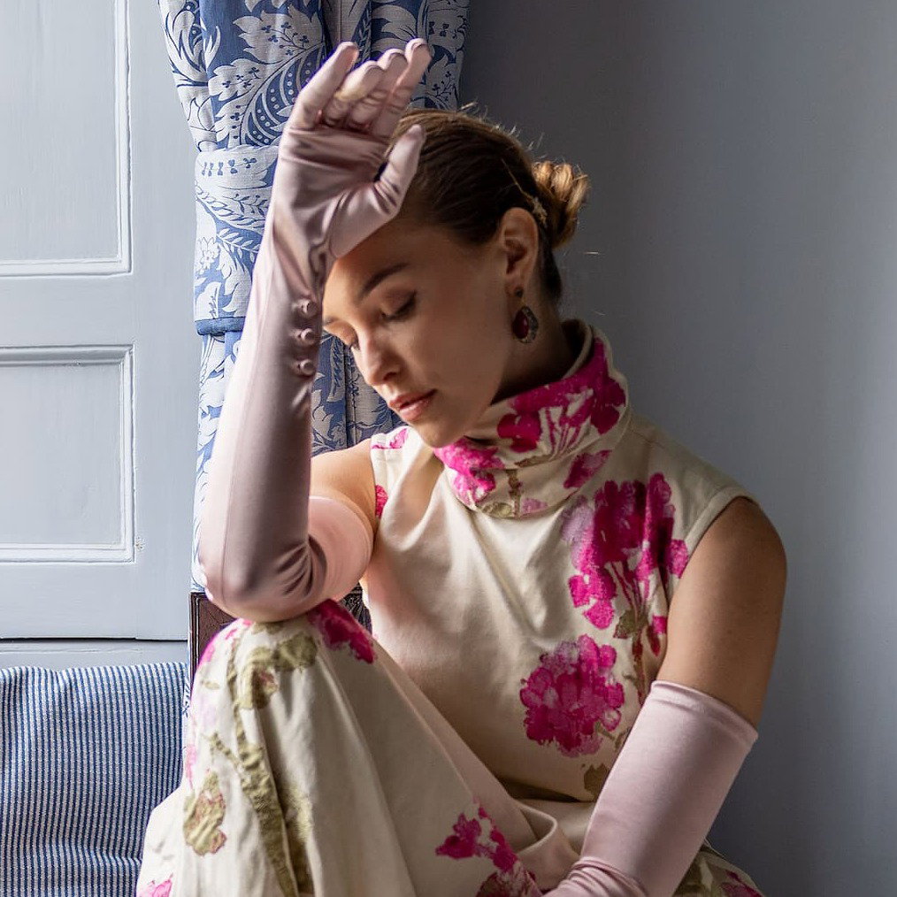 Woman wearing long satin gloves in rose sitting by the window