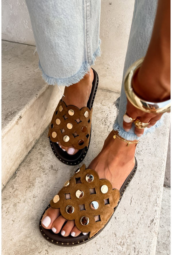 Brown suede scalloped slide sandals with circular mirror studs on feet with white pedicure, frayed hem jeans and gold anklet