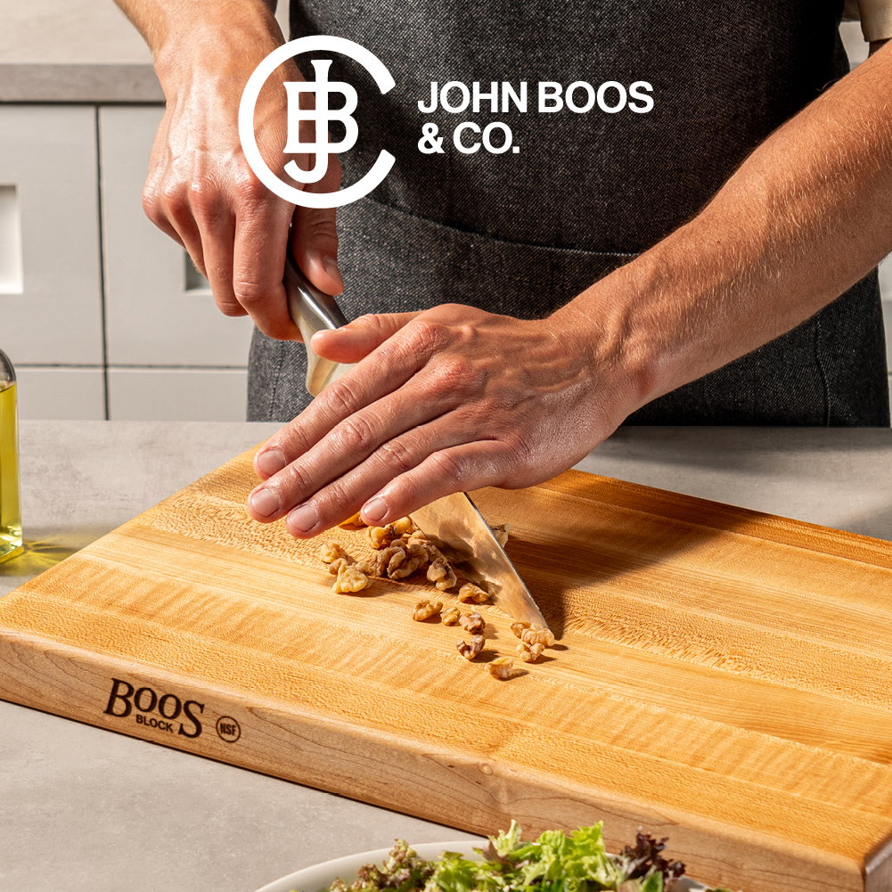 John Boos & Co. wooden cutting board in use with a chef slicing nuts, shown on a countertop with fresh ingredients nearby.