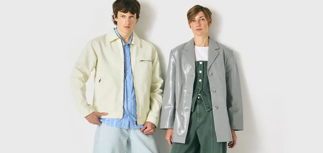 Zwei Models stehen vor einem weißen Hintergrund und tragen legere, übergroße Jacken: eine cremefarbene über einem blauen Hemd und die andere grau über einem grünen Outfit.