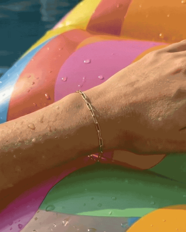 Woman's hand resting on an inflatable in a pool with gold paper clip bracelet on wrist 