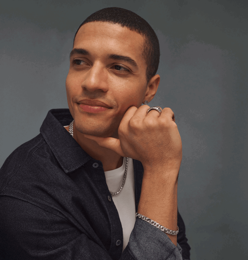 Male model wearing a thick silver chain, silver bracelet, signet ring and diamond stud earring.