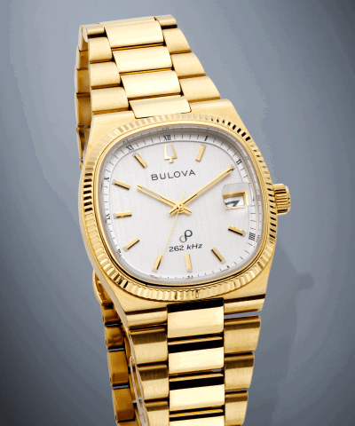 Gold-tone Bulova watch with a silver textured dial, fluted bezel and date window at 3 o’clock.