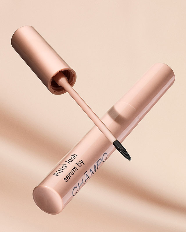 A pink eyelash serum tube with an open applicator brush, labeled 'Pitta lash serum by CHAMPO.'