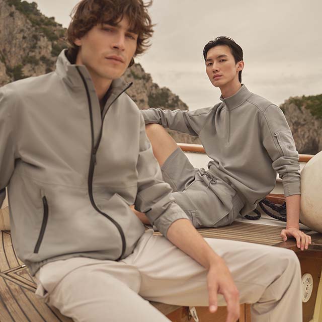 Two people in casual gray outfits on a wooden deck, with a rocky landscape in the background.