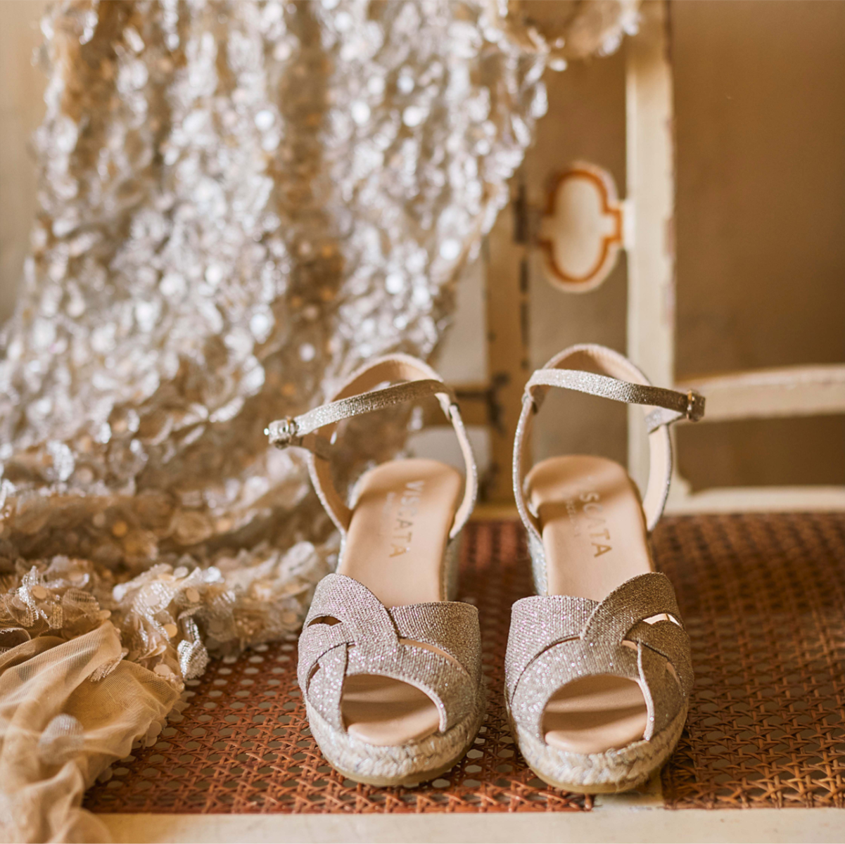 Champagne glitter Laia espadrille wedge sandals displayed on a woven chair beside soft lace fabric, with “The new icon” and “Discover Laia” text overlay.