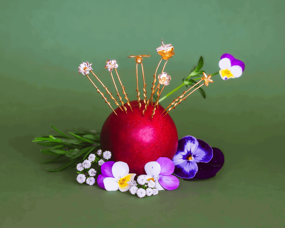 Set of 6 Mix Flower and Bee Small Hair Pins Summer Archive Sale jewellery styled in an apple with purple blooms against a green background.