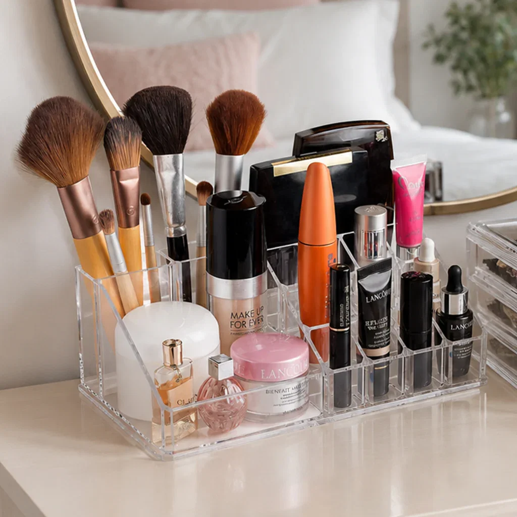 A clear acrylic makeup organizer displaying brushes, cosmetics, and skincare products on a bedroom vanity.
