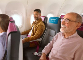 Dos hombres están sentados en un avión. En su fila hay un asiento central libre. Reserva ahora extras para el vuelo.