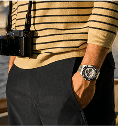 Man wearing a stainless steel chronograph watch with a striped sweater and camera.