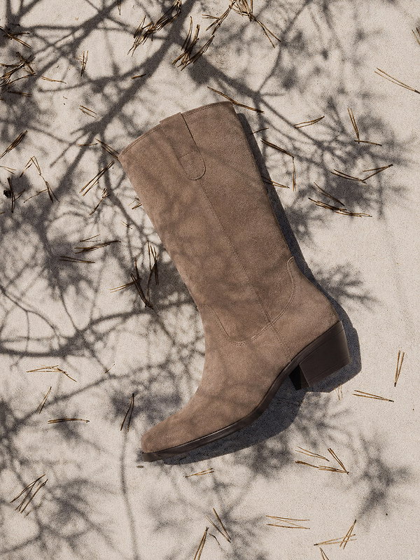 Brown suede boot on sandy ground with shadow of branches