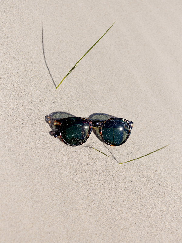 Sunglasses resting on sandy beach with blades of grass nearby