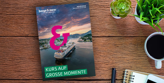 Neuer Kreuzfahrten-Katalog liegt auf einem Holztisch mit Blumen und Tasse Kaffee.