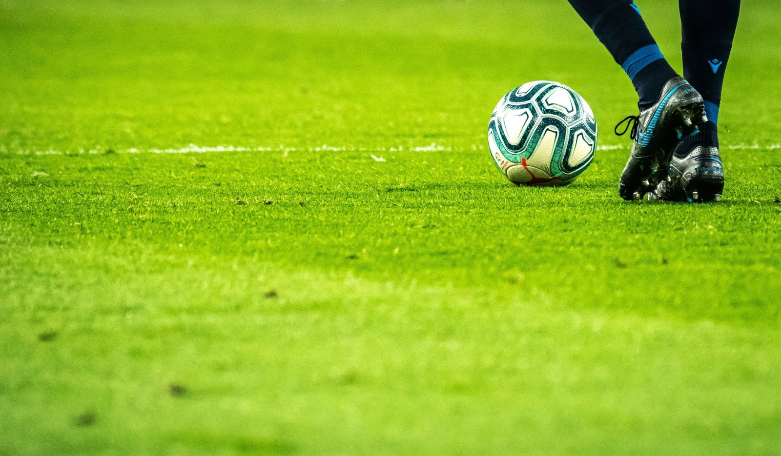 Premium lifestyle soccer image featuring a soccer ball on the pitch with a player preparing for play.