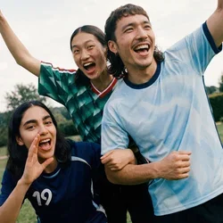 Drei junge Erwachsene in Sportbekleidung jubeln und lächeln im Freien in einem grasbewachsenen Park mit Bäumen im Hintergrund.