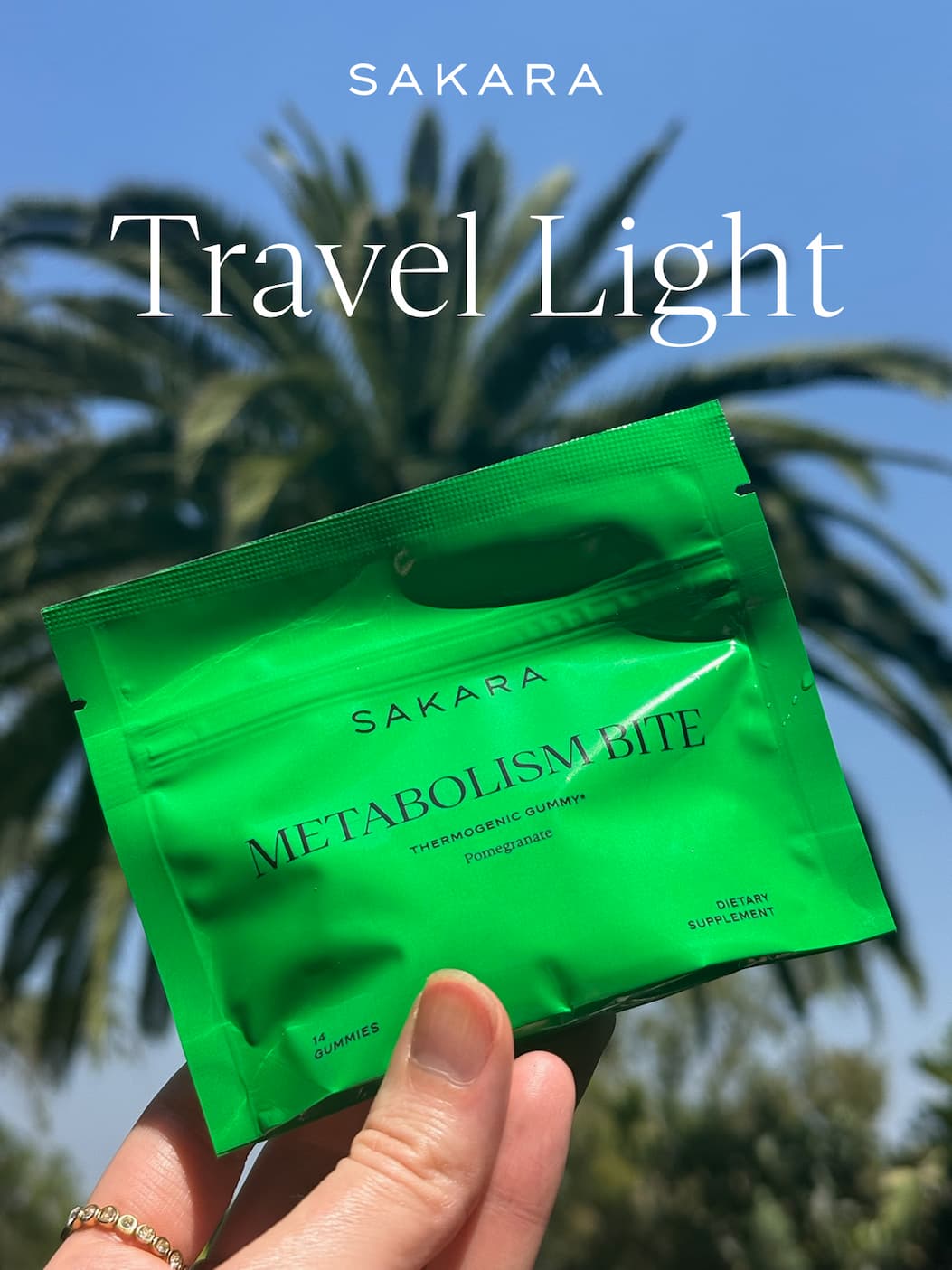 Hand holding a green Sakara Metabolism Bite pouch against a palm tree and blue sky, with text "Travel Light"