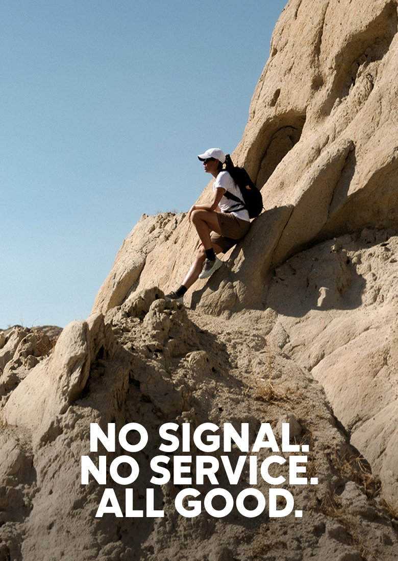 A hiker sitting on a rocky cliff looking out at the view. Headline reads No Signal. No Service. All Good. 