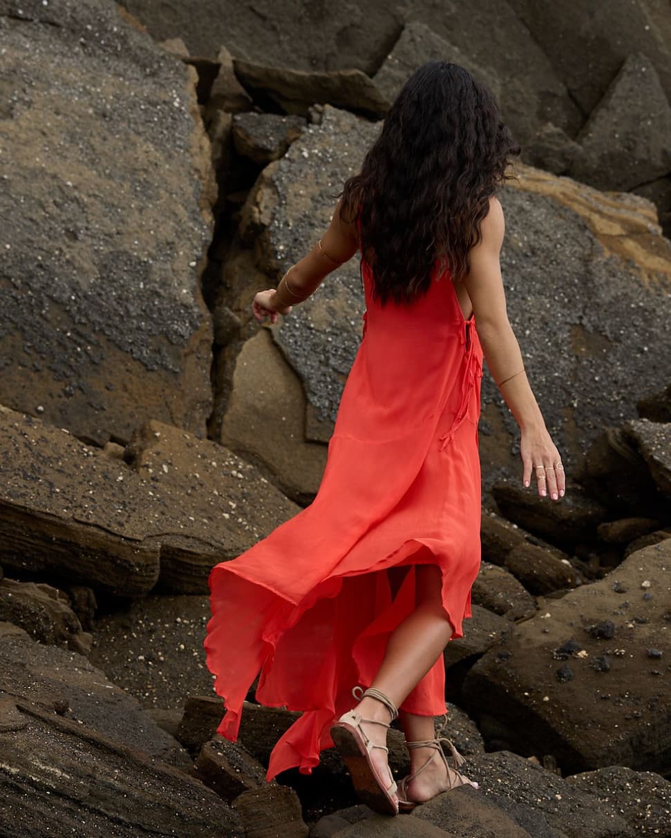 Woman wearing bright orange dress walking on rocks near the ocean