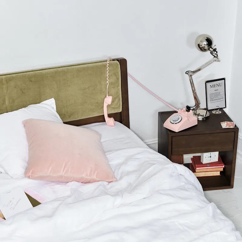 A bed with green velvet headboard and pink accent pillow next to nightstand with pink phone A bed with green velvet headboard and pink accent pillow next to nightstand with pink phone