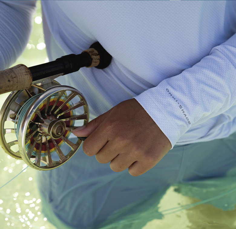 Close up of angler wearing omni-shade long sleeve while reeling in a fishing line.